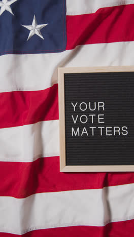 Vertikales-Video-Eines-Schildes-Mit-Der-Aufschrift-„Your-Vote-Matters“,-Das-Auf-Der-US-Flagge-„Stars-And-Stripes“-Für-Die-Amerikanische-Wahl-2024-Liegt-2